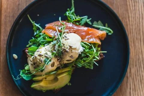 Egg benedict with arugula, salmon and avocado on a dark plate in the restaurant Stock Photos
