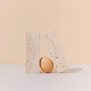 Egg between two travertine marble blocks on a beige and gray background. Stockfoto's