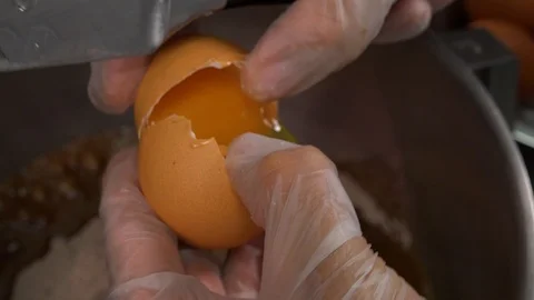 An egg is broken by a knife and the contents are dropped into a metallic bowl Stock-Footage 103098685