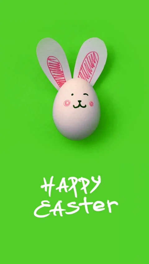 Egg with bunny face, paper rabbit ears, text Happy Easter on green background Stock Footage 310901783