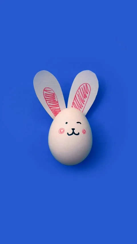 Egg with cute rabbit face and bunny ears on light cornflower blue Stock Footage 312512637