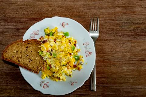 Egg dish with bacon, peppers, bread on a brown wooden table with fork Stock Photos