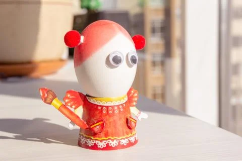 Egg for easter day. Egg is girl in the orange dress with eyes. Background close Stock Photos