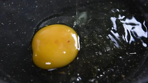 An egg falling on a black pan with olive oil Stock Footage 140029818