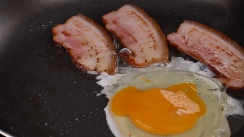 The egg falls on a hot frying pan with bacon Stock Footage 77520953