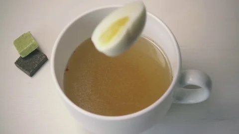 The egg falls into a white cup with clear soup. Slow motion Stock Footage 73740927