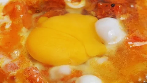An egg is fried in a frying pan with chopped tomatoes and onions. Close-up. Stock-Footage 297098757