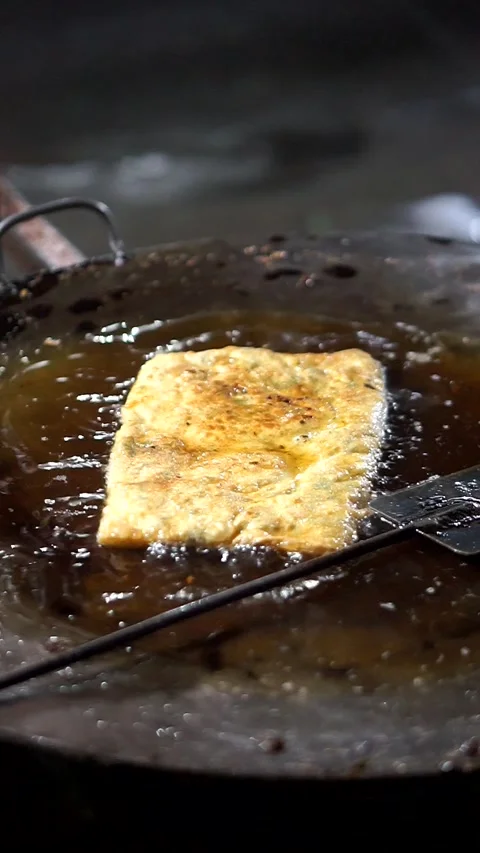 Egg martabak is fried in a large pan filled with hot oil as a traditional 動画素材 325513888