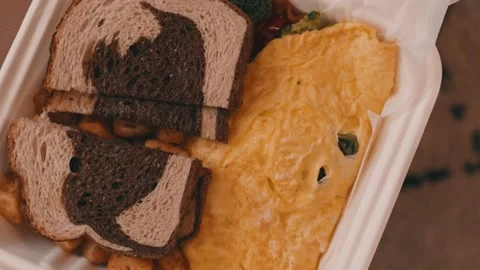 Egg Omelet, Homefries and Rye Toast in a takeout box on a wooden table in 4k Stock Footage 245452745