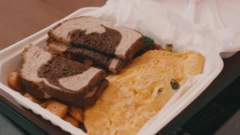Egg Omelet, Homefries and Rye Toast in a takeout box on a wooden table in 4k Stock Footage 245452968