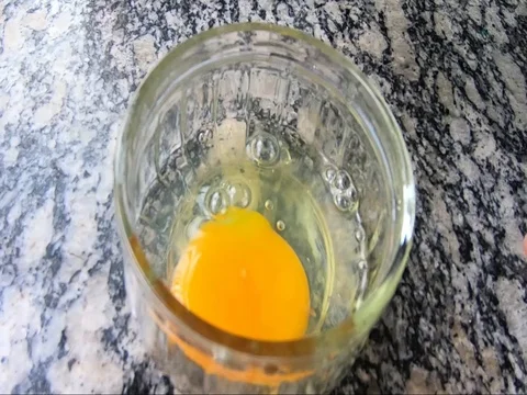 An egg opening and the yolk falling into a glass jar Stock Footage 94900340