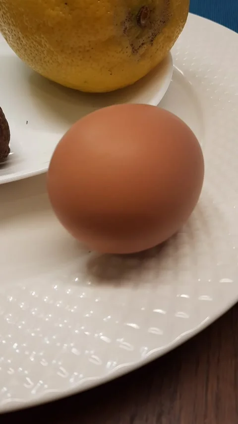 Egg rocking on plate next to lemon and nut Stock Footage 328452053