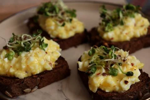 Egg salad on dark bread served on a plate with sprouts in a kitchen setting Stock Photos