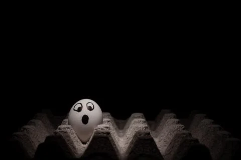 Egg with a scared face in its cardboard box. Black background. Free space to  Stock Photos
