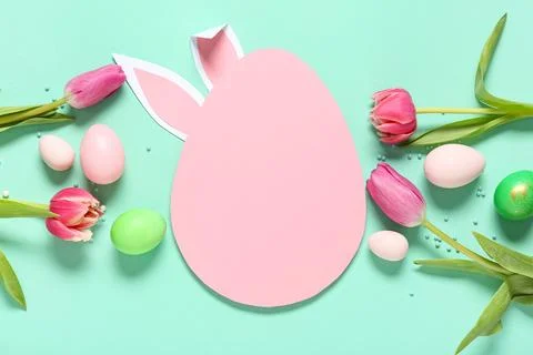 Egg-shaped blank card with paper bunny ears, Easter eggs, tulip flowers and b Stock Photos