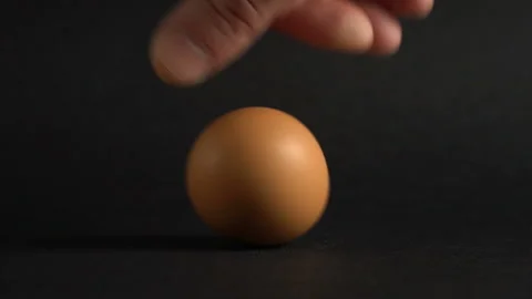 The egg spin by hand slow motion. A brown egg spinning on a black table. Stock Footage 103362139