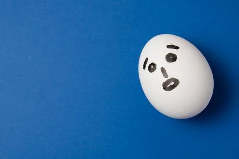 Egg with a surprised face on a blue background with copy space. Fotos Stock