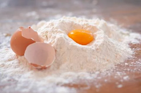 An egg yolk and an egg shell in flour on a wooden slab Stock Photos