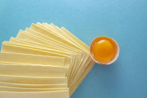 Egg yolk in a shell next to a high stack of raw lasagna sheets on blue back.. Foto stock