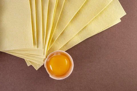 Egg yolk in a shell next to a high stack of raw lasagna sheets on brown bac.. Fotos de archivo