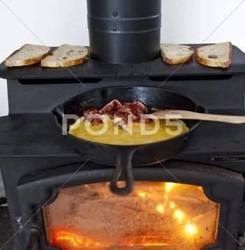 Eggs and Bacon Cooking in a Cast Iron Skillet on a Wood Burning Stove; Bread Stock Photos