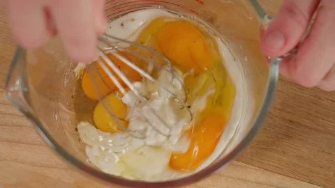 Eggs and milk are mixed with a girl's hands in a glass bowl with a whisk Stock Footage 253548966
