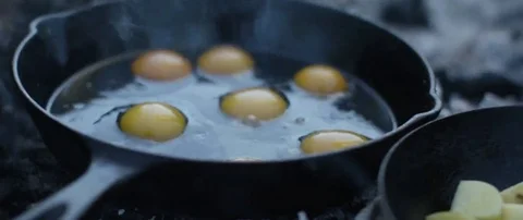 Eggs and potatoes being cooked in frying pan on campfire Stock Footage 69199687