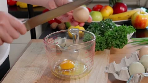 The eggs are broken into a glass measuring cup by the girl's hands. Stock Footage 253876033