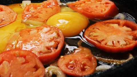 Eggs are cracked into a frying pan with tomatoes and onions. Medium shot. 库存影片 282905453