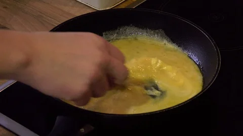 Eggs are poured into a hot pan and mixed to make an omelette Stock Footage 98981889