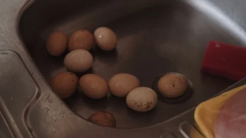 Eggs are washed in the sink in the kitchen, poured water into a saucepan Stock Footage 75638510
