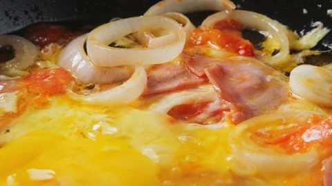 Eggs being cracked into a frying pan with tomatoes, ham and onions. Medium .. Stock Footage 284031669