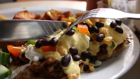 Eggs Benedict Black beans hashbrowns fork knife Stock Footage 126674563