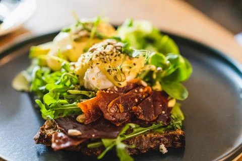 Eggs benedict with dried ham and salad mix on a black plate. Close-up view Stock Photos