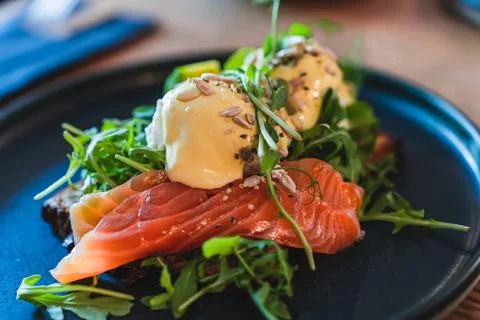Eggs Benedict with salmon and arugula on a black plate for breakfast in the Stock Photos