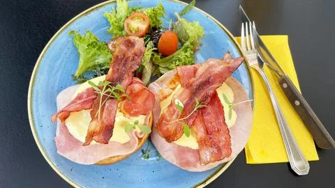 Eggs benedict served with crispy bacon, ham and hollandaise sauce on brioche bun Stock Photos