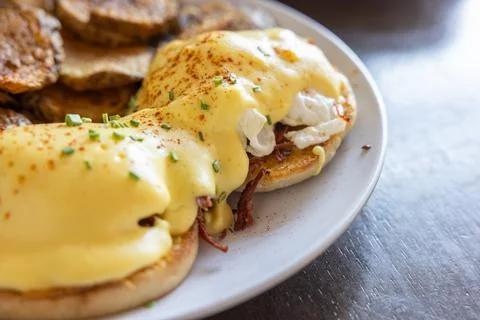 Eggs Benedict served with extra sauce and sliced potatoes. Stock Photos