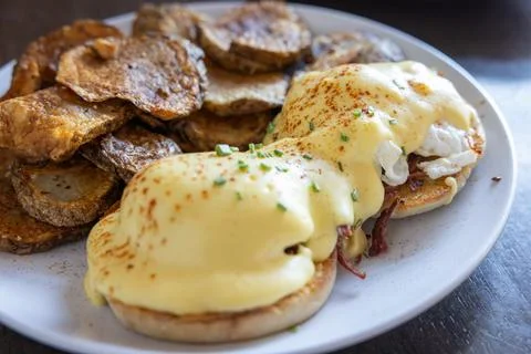 Eggs Benedict served with extra sauce and sliced potatoes. Stock Photos