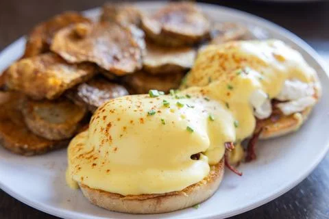 Eggs Benedict served with extra sauce and sliced potatoes. Stock Photos