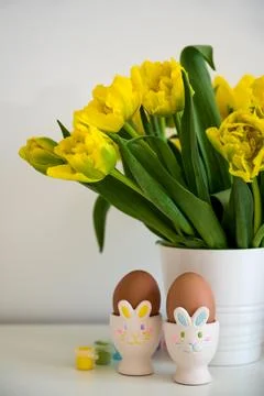 Eggs in bunny shaped egg cups near bunch of yellow tulips Stock Photos
