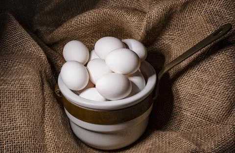 Eggs in a ceramic ladle on a burlap background. Stock Photos