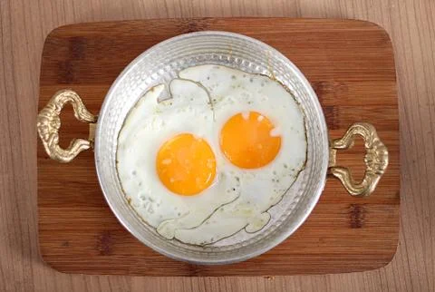Eggs cooked in oil in a high-angle copper dish Stock Photos