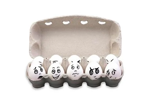 Eggs with different faces in a box isolated on white background. Stock Photos