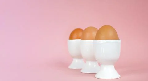 Eggs in egg cups on a pink background. Easter composition with copy space. Stock Photos