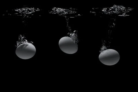 Eggs fall into the water on a black background Stock Photos
