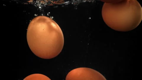 Eggs falling under water on a black background. Filmed on a high-speed camera at Stock Footage 322859059