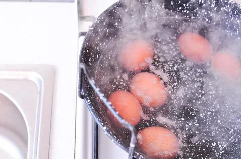 Eggs in shell in boiling water in black pot on the stove Stock Photos