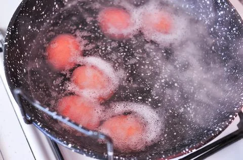 Eggs in shell in boiling water in black pot on the stove Stock Photos