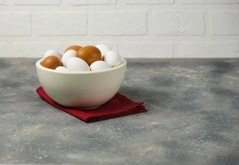 Eggs in a white ceramic bowl on a red napkin on the gray surface of the table Stock Photos