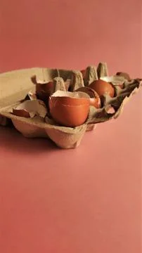Eggshell halves in recycled cardboard packaging on a pink background. Broken Stock Photos